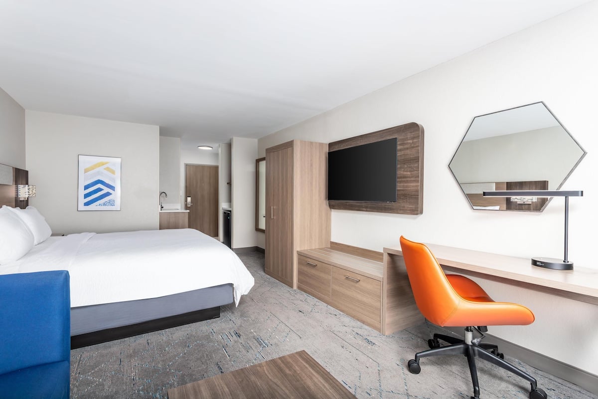 A hotel room with a bed, a desk, a chair, a TV, and a mirror.
