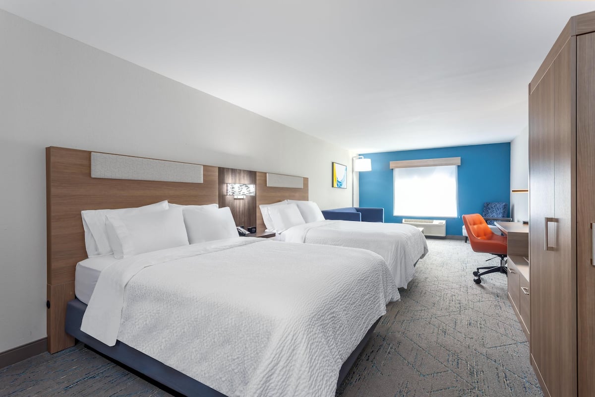 A hotel room with two beds, a desk, an orange chair, and a wardrobe.