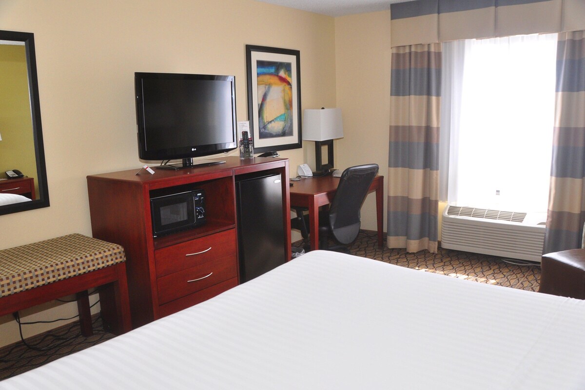 Quarto de hotel com cama, escrivaninha, televisão, micro-ondas, cadeira e ar condicionado.