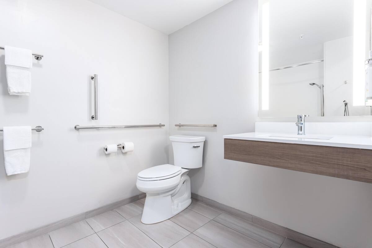 A modern bathroom with a toilet, handrails, a sink, and a mirror.