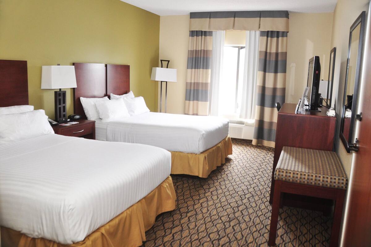 A hotel room with two beds, a desk with a computer, a chair, and a window with curtains.