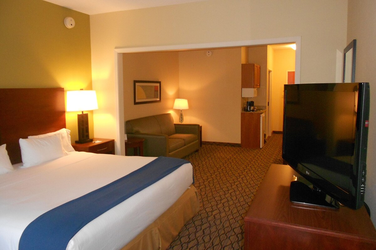 Quarto de hotel com cama, televisão, escrivaninha e cozinha compacta.