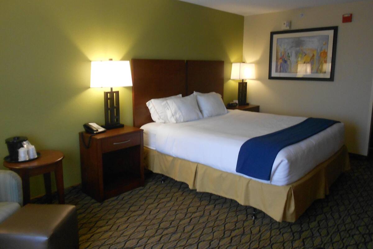 A hotel room with a large bed, two bedside tables, a chair, a lamp, and a painting on the wall.