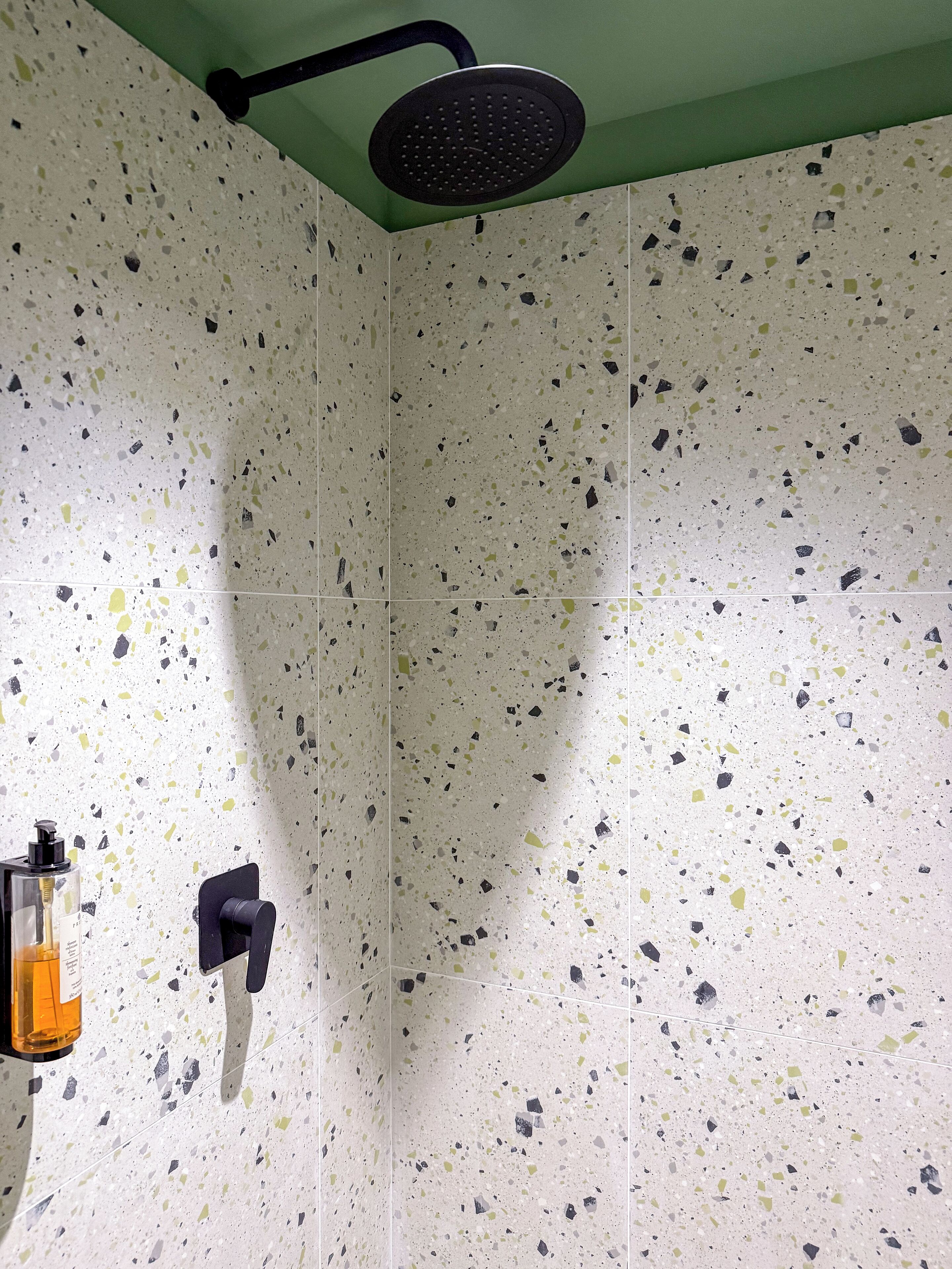 Een douche met een zwarte douchekop, een zeepdispenser en een wand met puntmotief tegels.