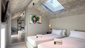 Un dormitorio moderno con dos camas, un tragaluz, un cuadro y un televisor en la pared.