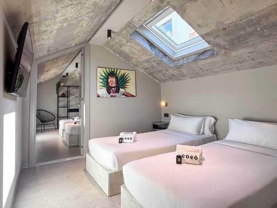 Un dormitorio moderno con dos camas, un tragaluz, un cuadro y un televisor en la pared.