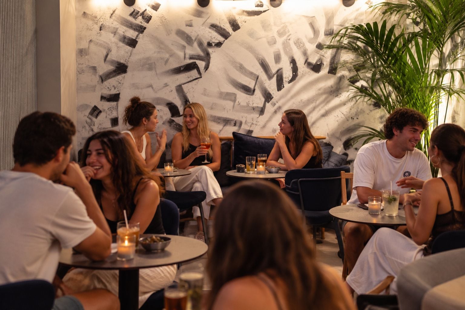 Un grupo de personas sentadas en mesas redondas en un restaurante con un diseño de arte abstracto en la pared.
