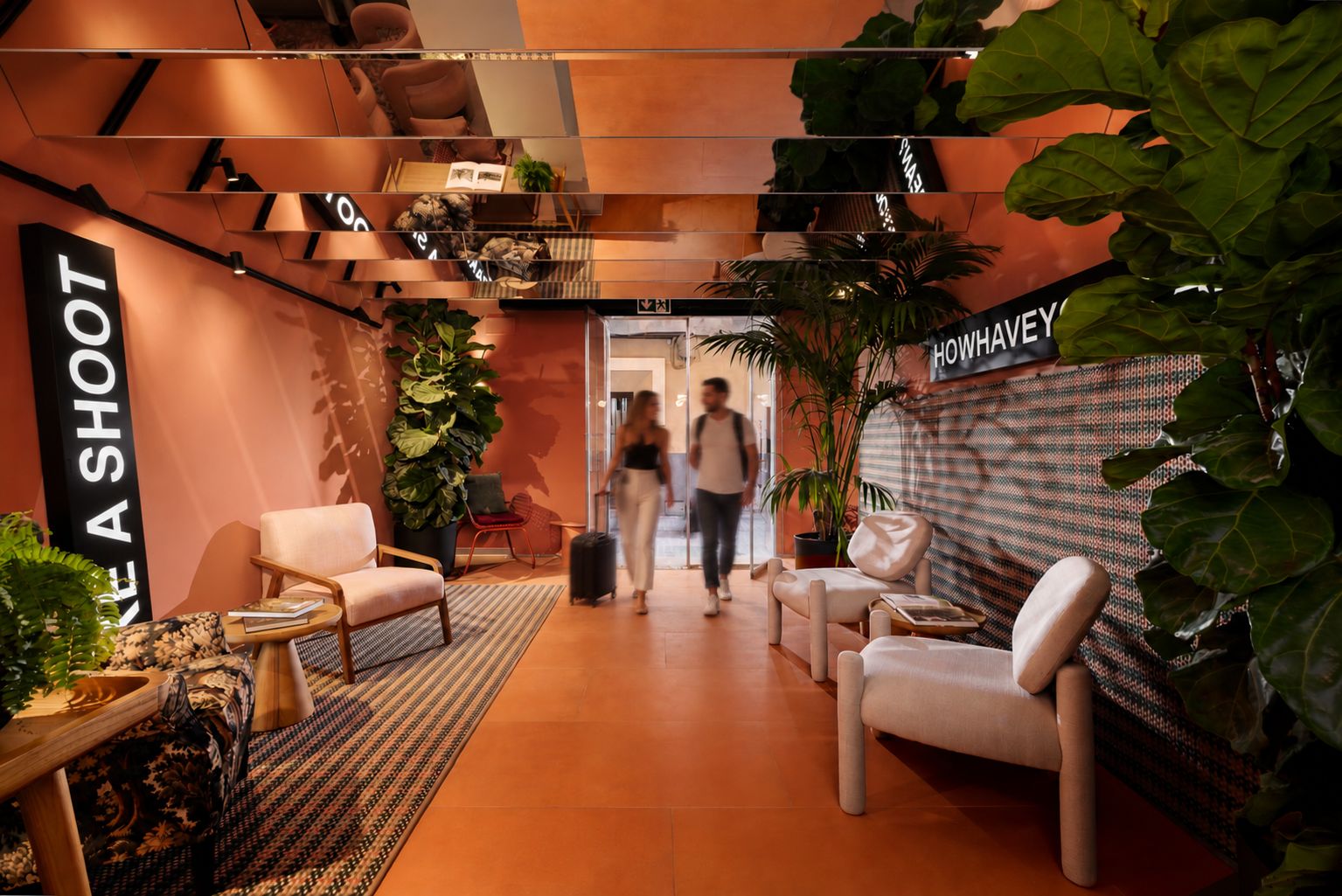 A modern lounge area with seating, a large plant, and a sign reading 'MAKE A SHOUT'.