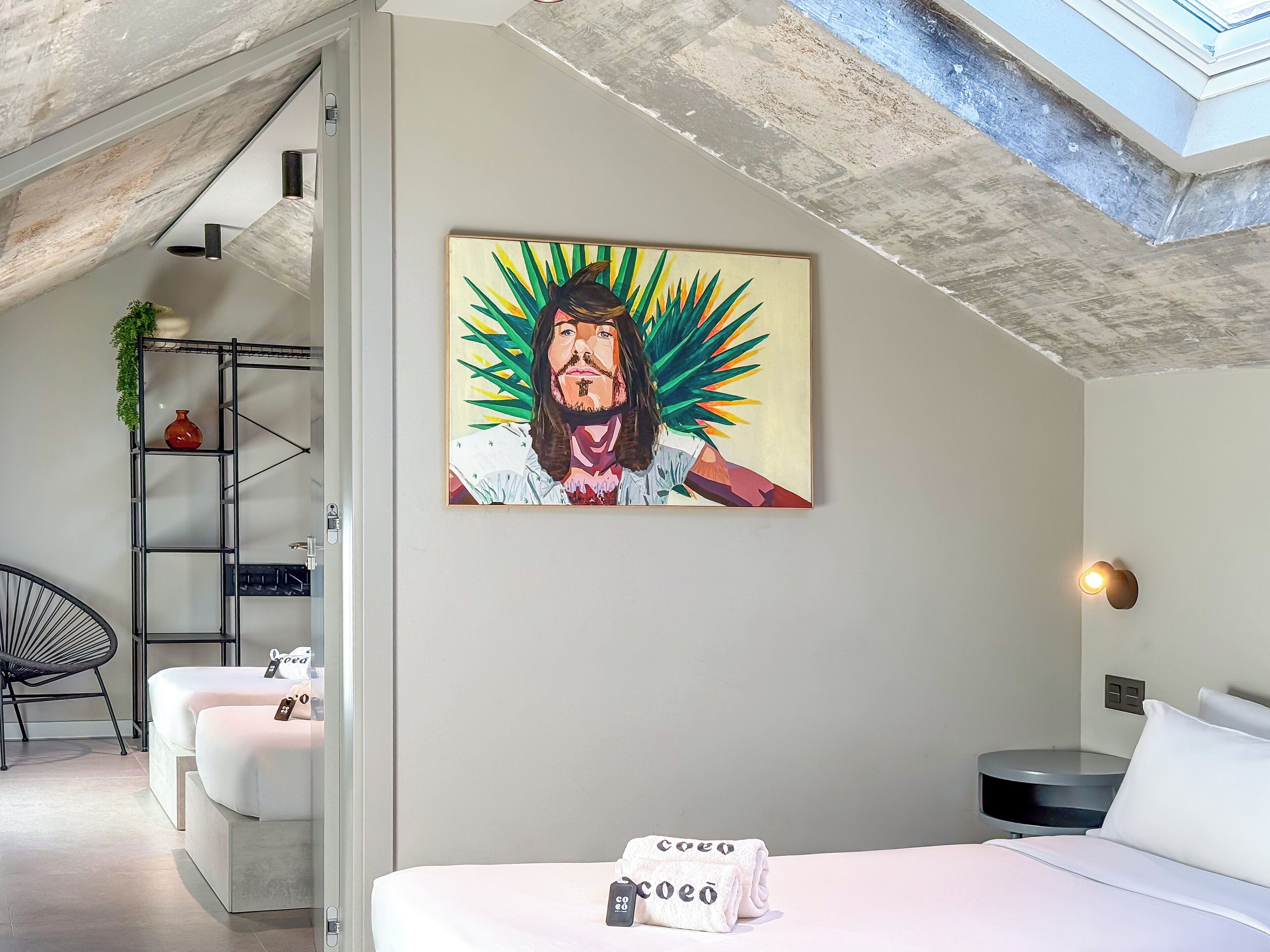 A modern hotel room with a bed, a wall-mounted painting, a side table, and a chair.