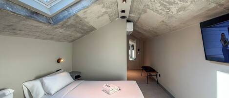 A compact bedroom with two beds, a skylight, a small desk, and a television.