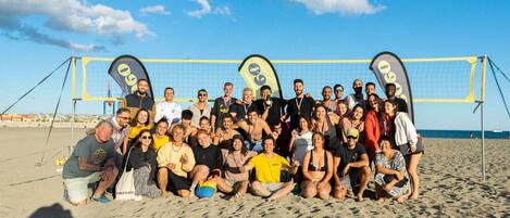A group of people on a beach with a volleyball net in the background.