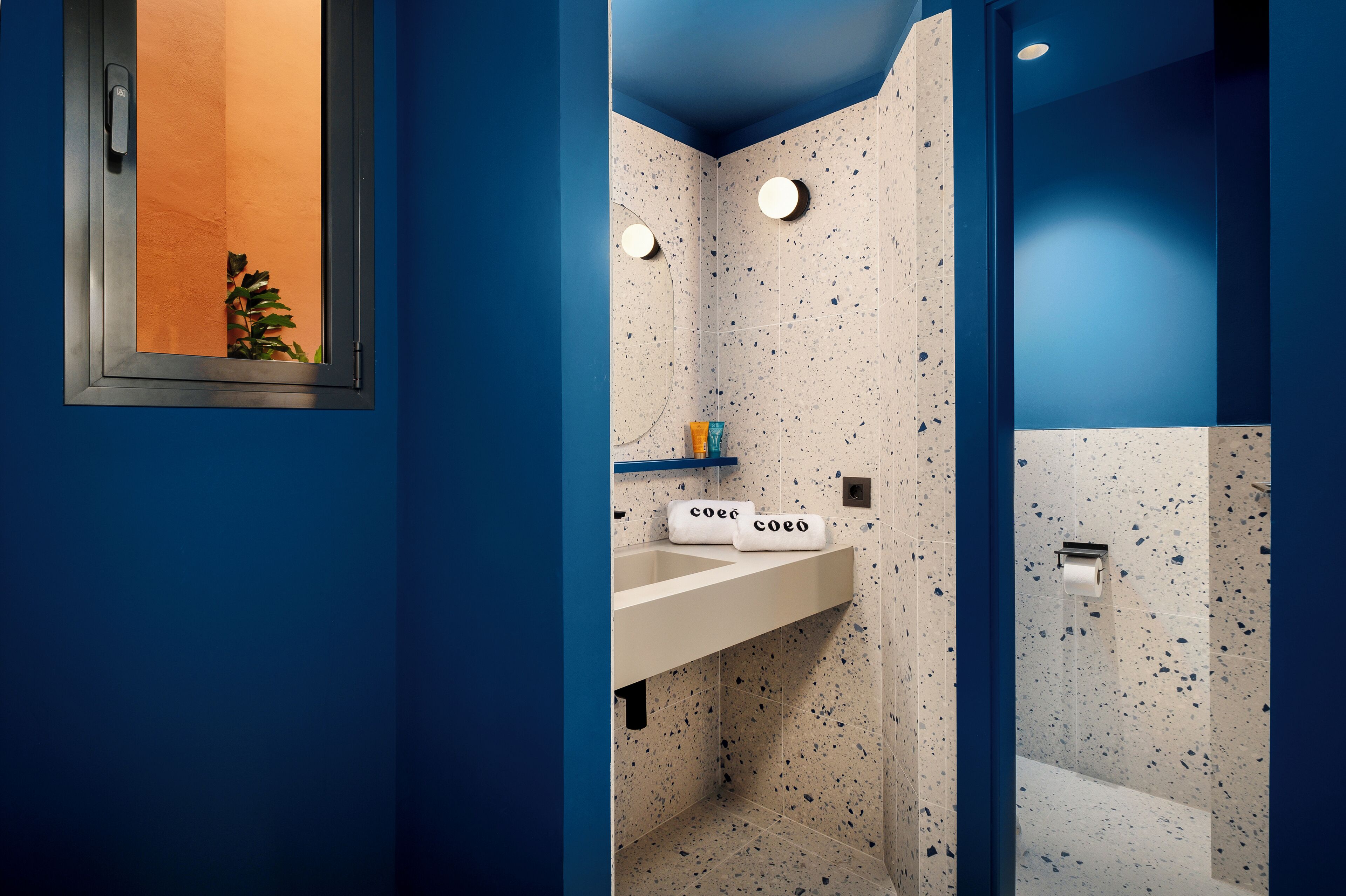 A bathroom with a blue and white speckled tile design, a white sink, and a towel rack with towels labeled "coeo".