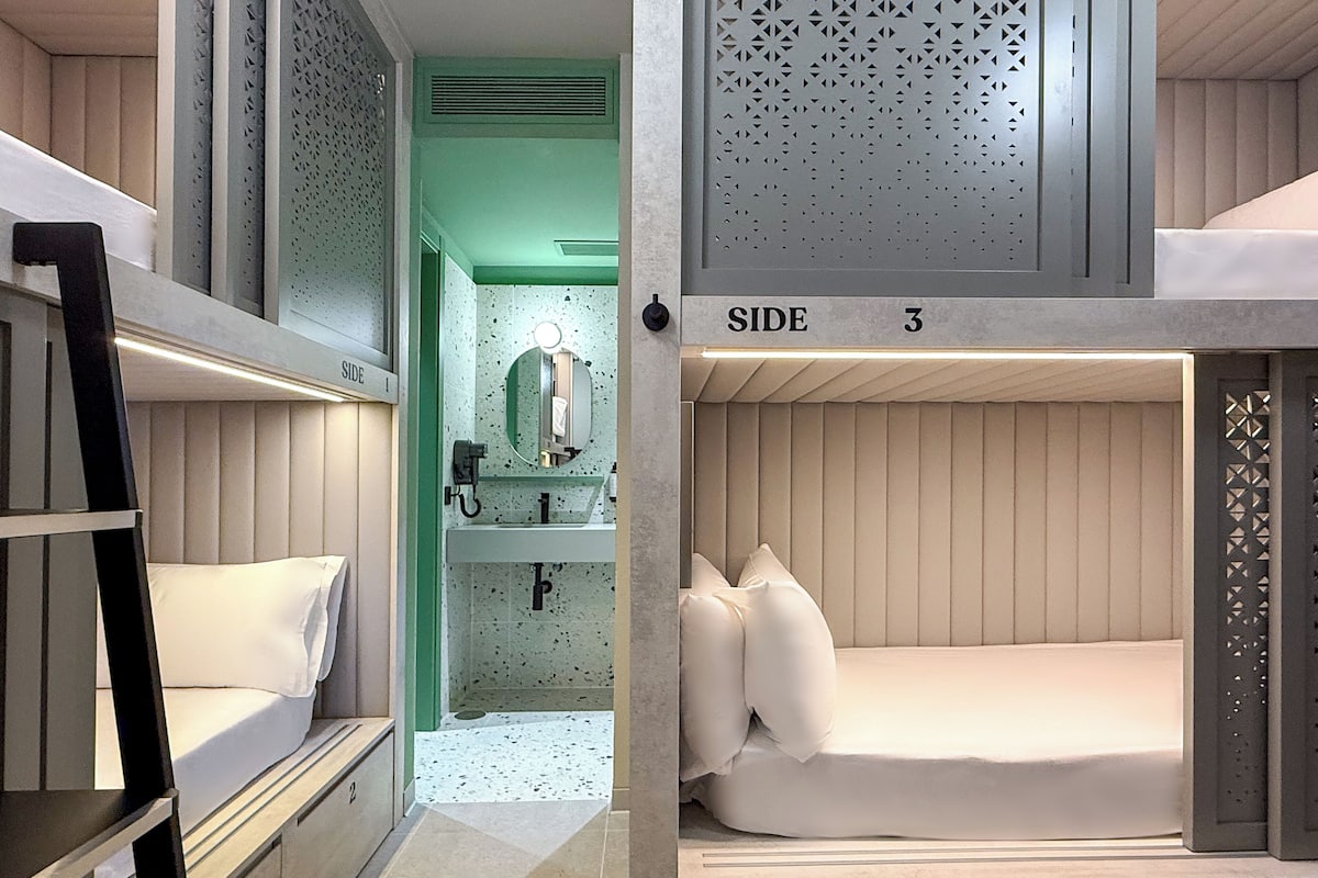 Een slaapkamer met stapelbed, een groene accentmuur, een wastafel en een spiegel.