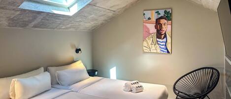 A modern bedroom with a skylight, a bed with white linens, a black chair, and a painting on the wall.