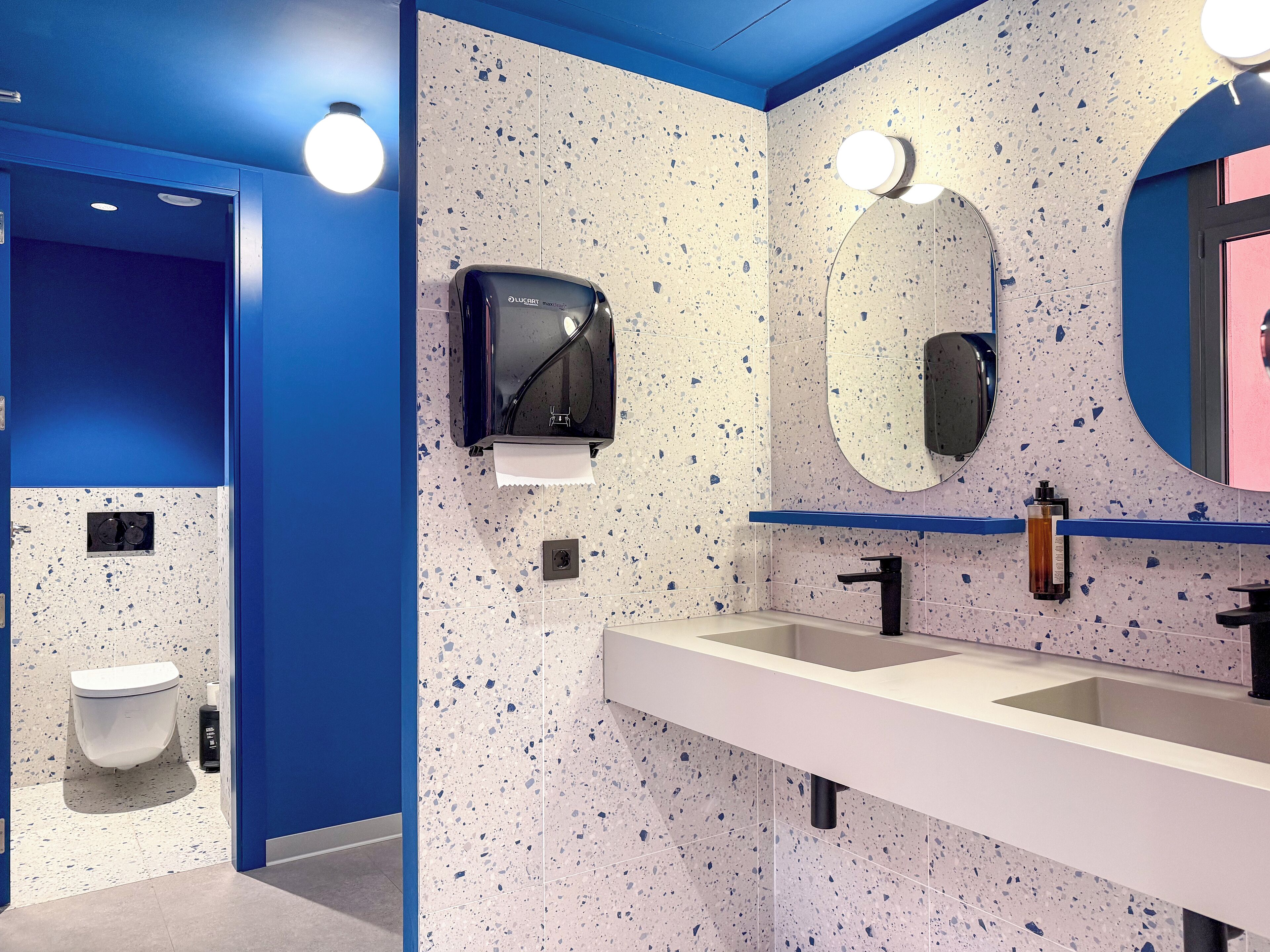 A modern bathroom with a blue accent wall, a hand dryer, a sink, and a mirror.