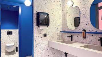 A modern bathroom with a blue accent wall, a hand dryer, a sink, and a mirror.