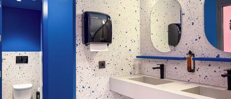 Un baño moderno con una pared azul de acento, un secador de manos, un lavabo y un espejo.