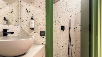 Une salle de bain dotée d’un grand lavabo blanc, d’une douchette à main et d’un distributeur de savon fixé au mur.