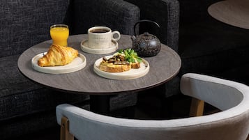 Una mesa redonda con un desayuno que incluye un croissant, tostadas y una tetera.
