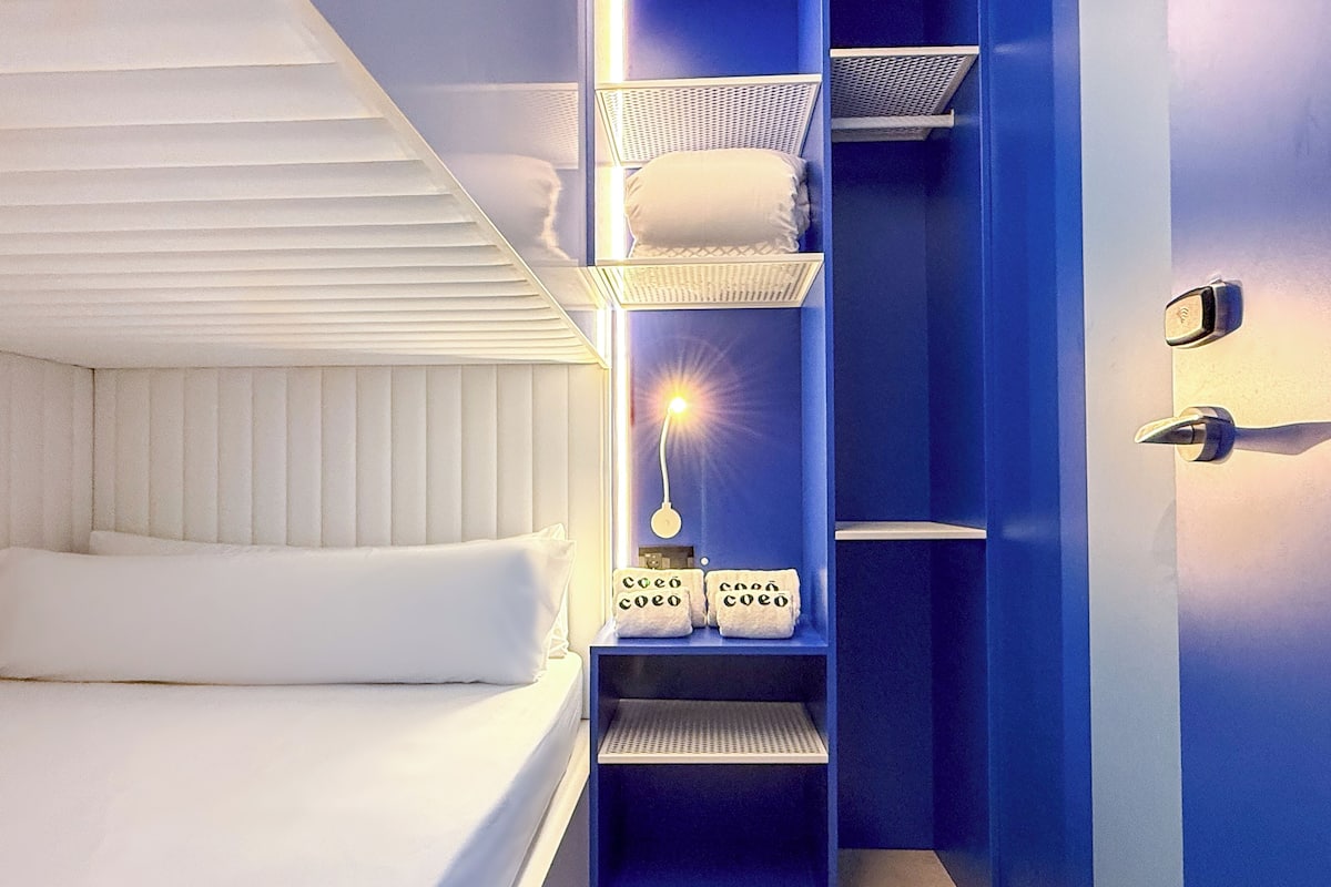 Een moderne slaapkamer met een stapelbed, een nachtkastje met een lamp en een garderobe met planken.
