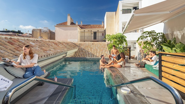 Zona de piscina con gente relajándose y sentada alrededor.