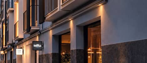 A hotel exterior with a sign for a brunch restaurant, a balcony with a wrought iron railing, and a decorative wall-mounted light fixture.