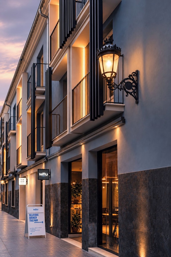 Exterior de un hotel con un letrero para un restaurante de brunch, un balcón con barandilla de hierro forjado y un accesorio de luz decorativo montado en la pared.