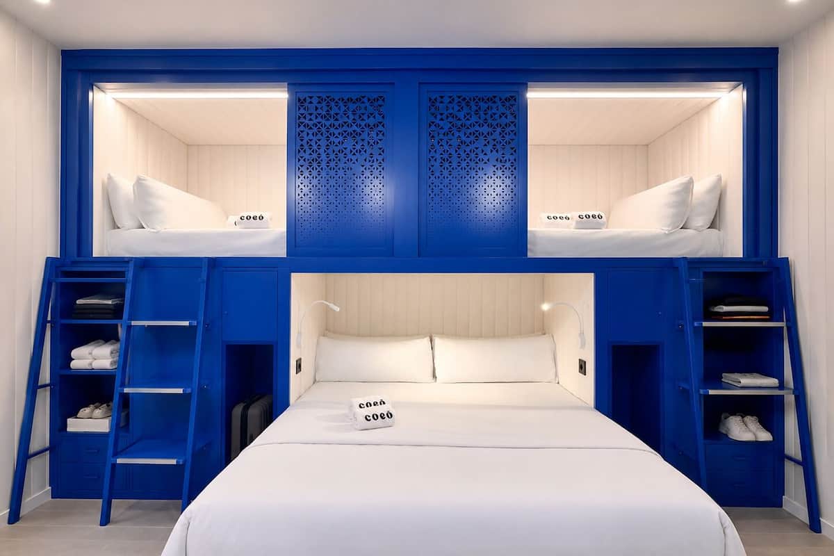 Een slaapkamer met stapelbedden, een blauw kleurenschema, witte beddengoed en een klein nachtkastje met een lamp.