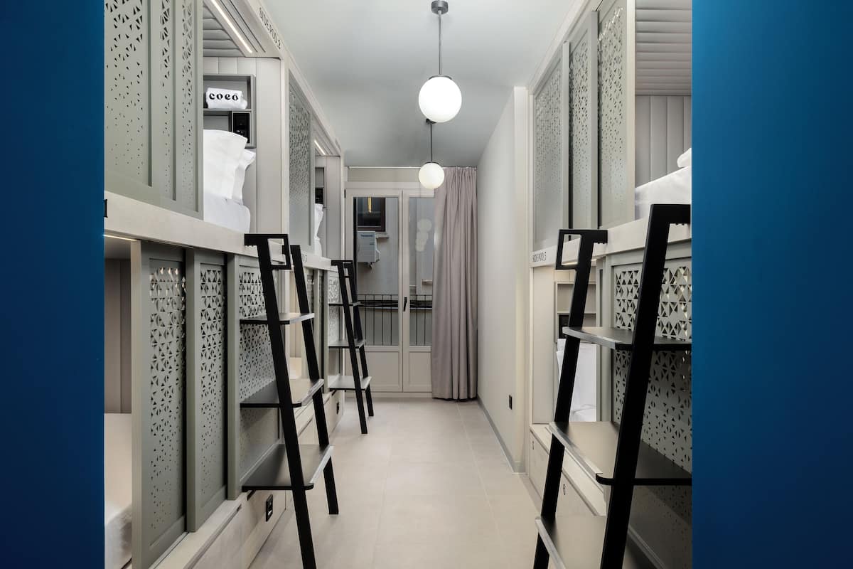 Een smalle gang met stapelbedden, een ladder en een deur naar een badkamer.