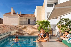 Una piscina con gente relajándose e interactuando, rodeada de edificios y vegetación.