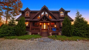 Una casa grande de madera oscura con un porche delantero notable, múltiples ventanas y un camino de piedra que conduce a la entrada.
