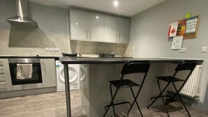 Een moderne keuken met een centraal eiland, twee zwarte barkrukken, een roestvrijstalen afzuigkap en een inbouwoven.