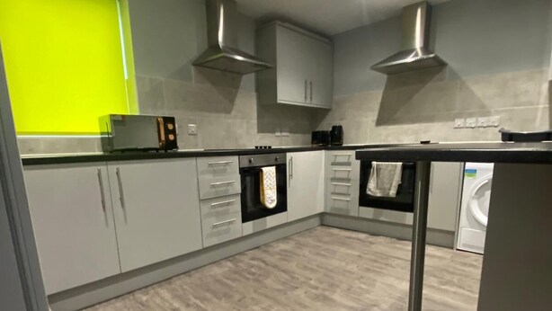 Een moderne keuken met grijze kastjes, roestvrijstalen apparatuur en een felgele accentmuur.
