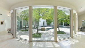 Un interior moderno con grandes puertas de cristal que dan a un patio exterior con piscina, rodeado de árboles.