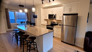 A modern kitchen with white cabinets, stainless steel appliances, and a central island with bar stools. - rent comfort in canmore - central to everything (Canmore)
