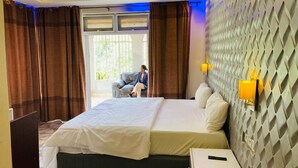 A hotel room with a large bed, a desk, a chair, and a view of the outdoors. - Emerald Villa Cafe & Restaurant (Kigali)