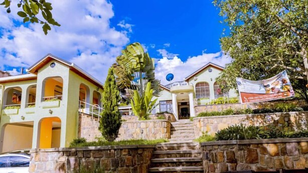 A residential building with a stone staircase leading to a front door, surrounded by greenery and a clear blue sky. - Emerald Villa Cafe & Restaurant (Kigali)
