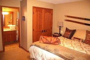 Une chambre d’hôtel avec une armoire en bois, un lit avec une literie à motifs, une table de chevet avec une lampe et deux paires de skis accrochés au mur.