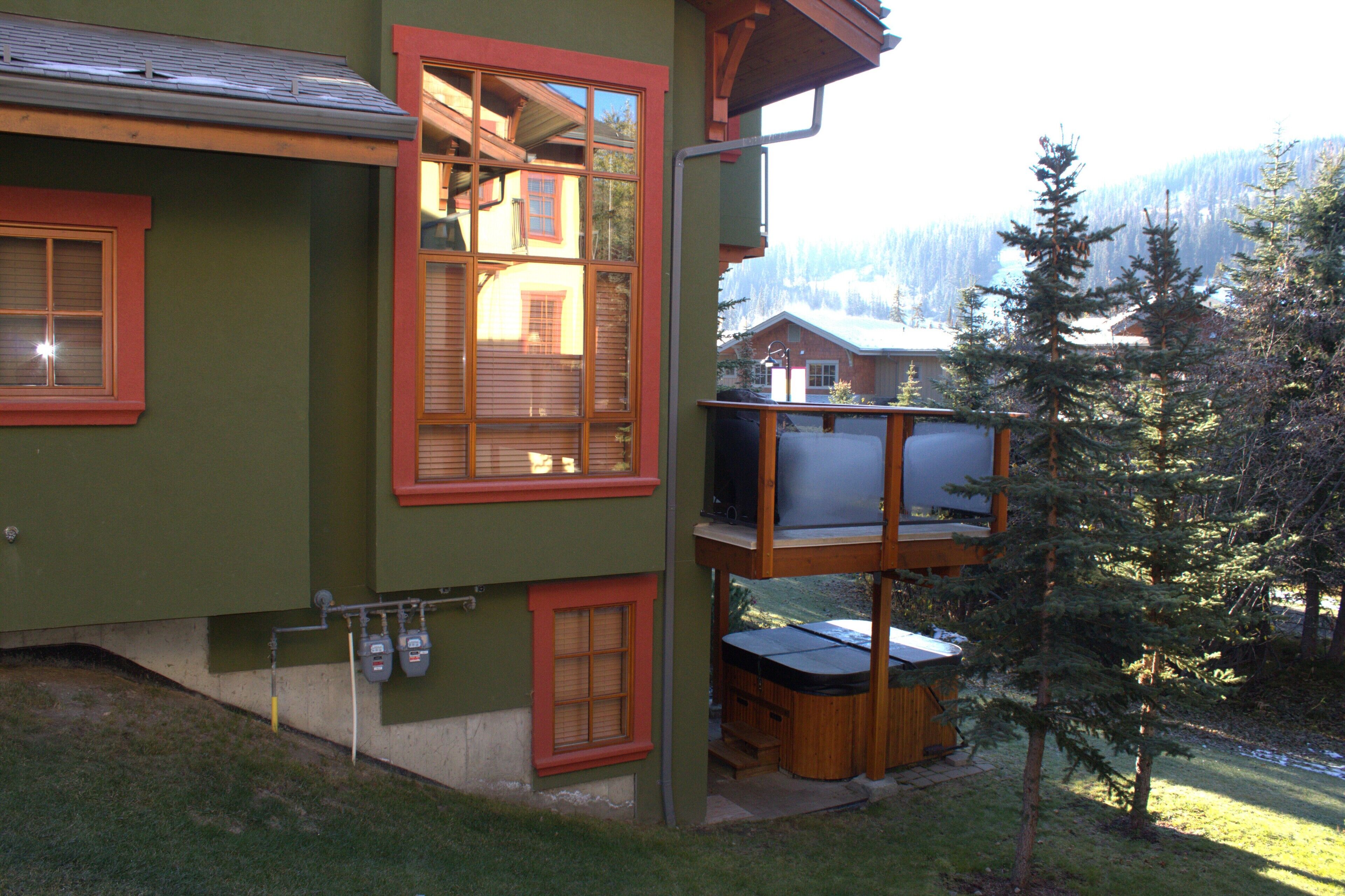 A two-story building with a balcony, a hot tub, and a view of a forested mountain.