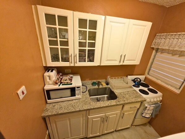 A compact kitchen with white cabinets, a microwave, a sink, and a stove. - Harmony Studio - Charming 1-bedroom in peaceful Tower Isle with AC, WiFi (Tower Isle)