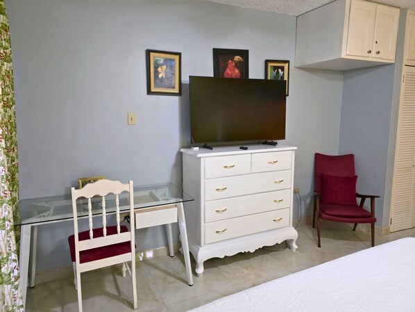 A bedroom with a bed, a desk with a chair, a dresser, and a television on top. - Harmony Studio - Charming 1-bedroom in peaceful Tower Isle with AC, WiFi (Tower Isle)
