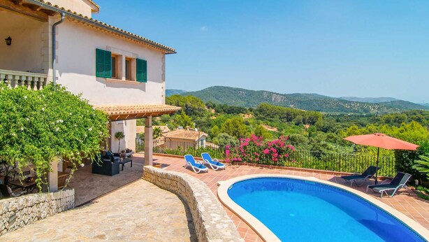 A villa with a swimming pool, outdoor seating, and a view of the surrounding hills.