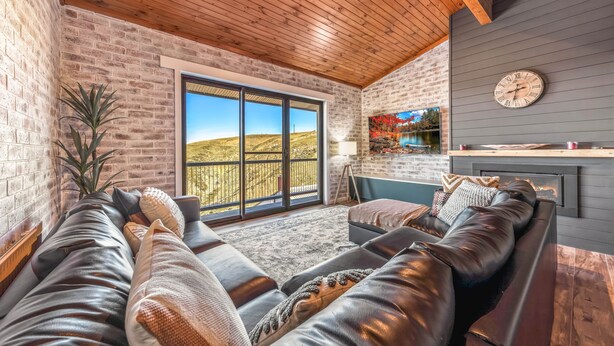 A modern living room with a leather sofa, a fireplace, and a large window offering a view of the countryside.