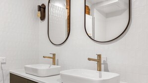 A modern bathroom with two sinks, a mirror, and a light fixture.