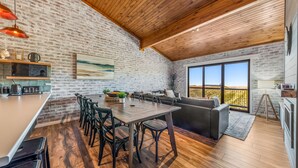 A modern kitchen with a brick wall, wooden ceiling, and a large window.