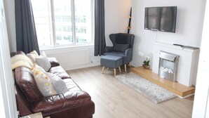 A modern living room with a leather sofa, a grey armchair, a flat-screen TV, and a fireplace.