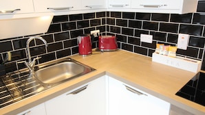 A modern kitchen with a stainless steel sink, a red kettle, a toaster, and a tea station.