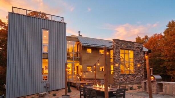 A modern house with a stone exterior, a metal structure, and a fire pit area. - Luxe Lakefront Estate near Minneapolis, Hot Tub, Sauna, Kayaks, Sleeps up to 20 (Baldwin)