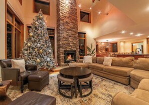 A spacious living room with a large Christmas tree, a stone fireplace, leather sofas, and a round coffee table.