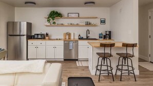 Una cocina moderna con armarios blancos, un refrigerador de acero inoxidable, lavavajillas e isla de madera con taburetes de bar.